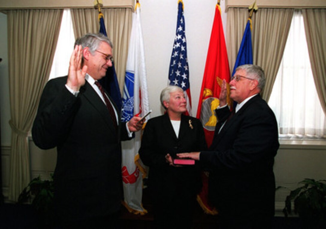 Deputy Secretary of Defense John J. Hamre (left) administers the oath of office to Art Money (right) as Assistant Secretary of Defense for Command, Control, Communications and Intelligence, as Money's wife Sharon holds the bible in a Pentagon ceremony on Oct. 5, 1999. 