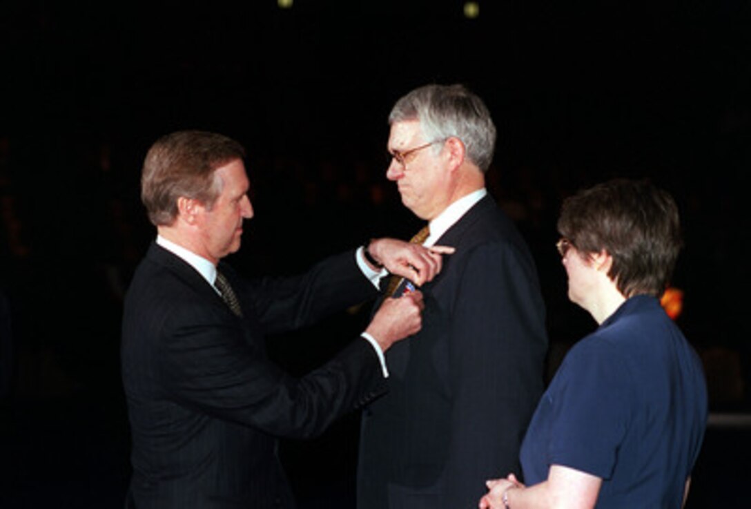 Secretary of Defense William S. Cohen (left) presents the Department of Defense Distinguished Public Service Medal to departing Deputy Secretary of Defense John J. Hamre (center) as his wife Julie (right) watches during ceremonies at Conmy Hall, Fort Myer, Va., on March 30, 2000. Hamre has served as the 26th Deputy Secretary of Defense since July 29, 1997. 