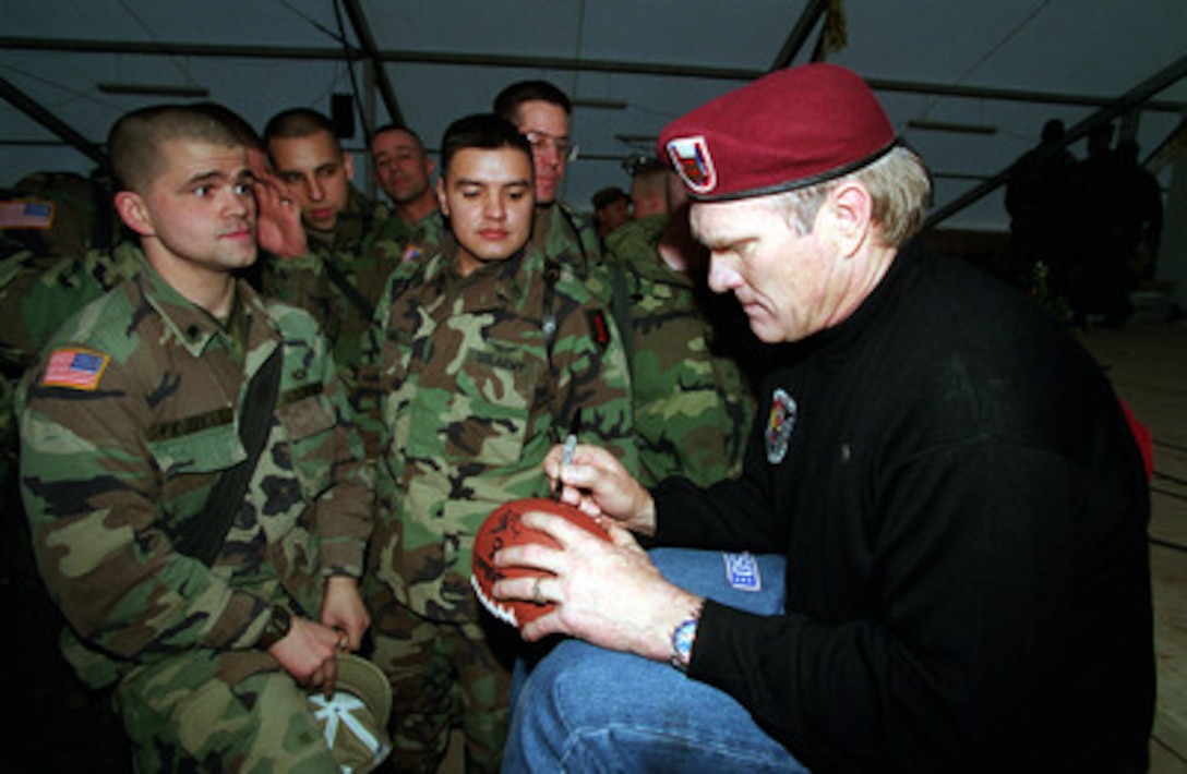 Former Steelers quarterback and Fox Television sports commentator Terry Bradshaw wears a beret of the 82nd Airborne as he autographs a football for a soldier during a United Service Organizations (USO) show at Camp Bondsteel, Kosovo, on Dec. 23, 1999. Bradshaw joined the entourage of entertainers, cheerleaders, sports figures, and comedians accompanying Secretary of Defense William S. Cohen on his third annual holiday tour and USO show. 