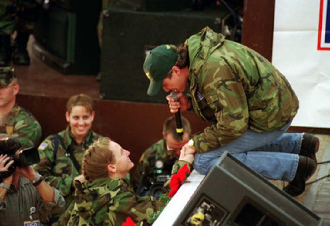 Country singer Shane Minor (right) sings to U.S. Army Spc. Jennifer Miller (center) during a United Service Organizations (USO) show in the Eagle Sports Complex at Tuzla Air Base, Bosnia and Herzegovina, on Dec. 22, 1999. Minor joined the entourage of entertainers, cheerleaders, sports figures, comedians and a super model accompanying Secretary of Defense William S. Cohen on his third annual holiday tour and USO show. Miller, from Gettysburg, Pa., is attached to Company H, 104th Aviation Regiment. 