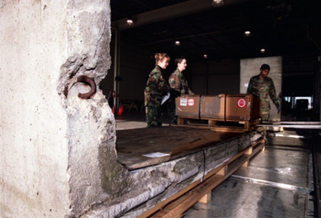 Senior Airmen Pamela Devine, Shanna Hooker and Airman Nina Roulhac remove a pallet of cargo sitting on a section of the Berlin Wall at Dover Air Force Base, Del., on Jan. 3, 2000. Two sections of the wall were docked at Dover waiting for shipment to Wright-Patterson Air Force Base, Ohio, where they will be displayed in the Air Force Museum. The airmen are attached to the 436th Aerial Port Squadron at Dover. 