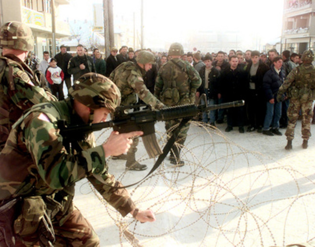 Soldiers of the 504th Parachute Infantry Regiment uncoil two rows of concertina wire to maintain crowd control as residents of Vitina, Kosovo, protest in the streets on Jan. 9, 2000. The protesters were demanding the release of local Albanians held in custody for questioning. The soldiers are attached to the 82nd Airborne Division, Fort Bragg, N.C., and are deployed to Kosovo as part of KFOR. KFOR is the NATO-led, international military force in Kosovo on the peacekeeping mission known as Operation Joint Guardian. 
