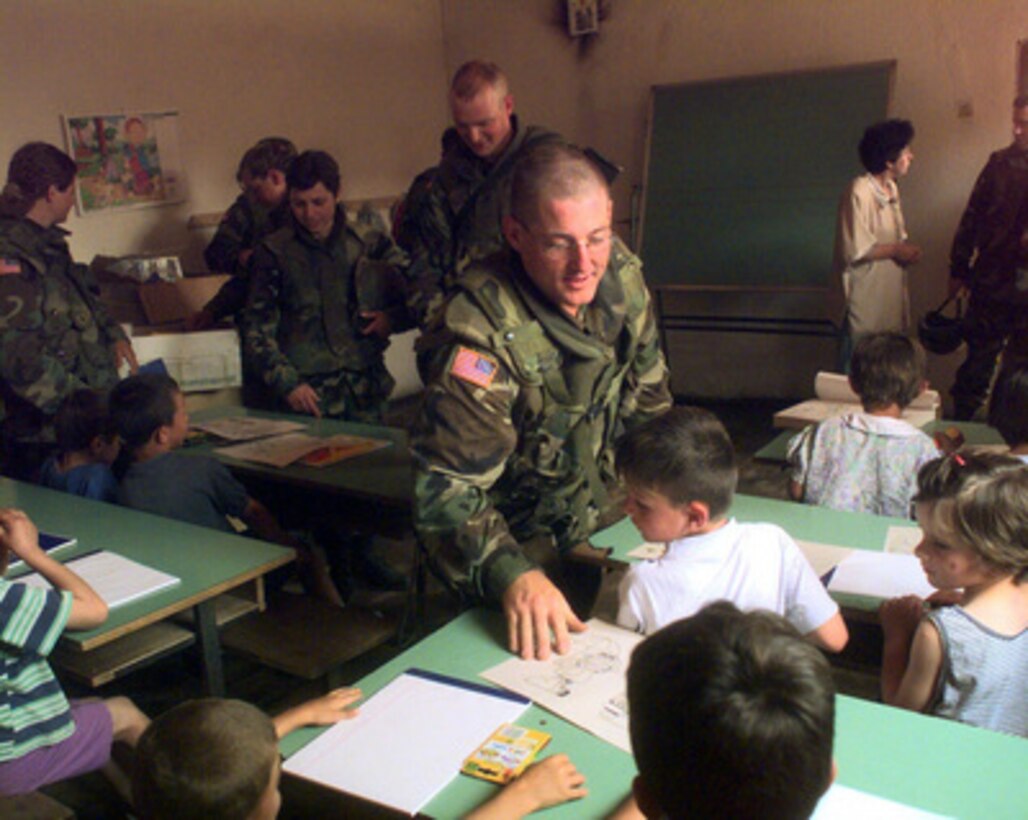 Spec. Jerry Qualley, of the North Dakota Army National Guard, hands out coloring book pages to students in a schoolhouse in Sodovina e Jerlive, a small Albanian village near Vitina, Kosovo, on May 19, 2000. Qualley and his fellow soldiers from Headquarters Support Company, 142nd Engineer Battalion, North Dakota Army National Guard, are delivering boxes of clothing and school supplies donated to the kids in this small village by the soldiers' families and churches back home. Soldiers of the 142nd are deployed to Kosovo, as part of KFOR. KFOR is the NATO-led, international military force in Kosovo on the peacekeeping mission known as Operation Joint Guardian. 