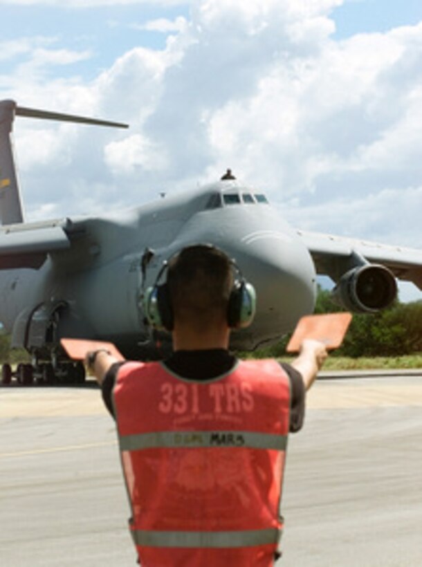 Airman 1st Class Andre Raymundo directs a U.S. Air Force C-5 Galaxy transport aircraft to a parking spot on the ramp at Hoedspruit Air Force Base, South Africa, on March 7, 2000. The Galaxy is delivering cargo, personnel and two HH-60 Pave Hawk helicopters from the 41st Rescue Squadron, Moody Air Force Base, Ga., for Operation Atlas Response. Operation Atlas Response is the U.S. military's contribution to relief efforts following torrential rains and flooding in southern Mozambique and South Africa. Raymundo is a crew chief assigned to the 436th Aircraft Generation Squadron. The Galaxy is deployed from the 436th Airlift Wing, Dover Air Force Base, Del. 