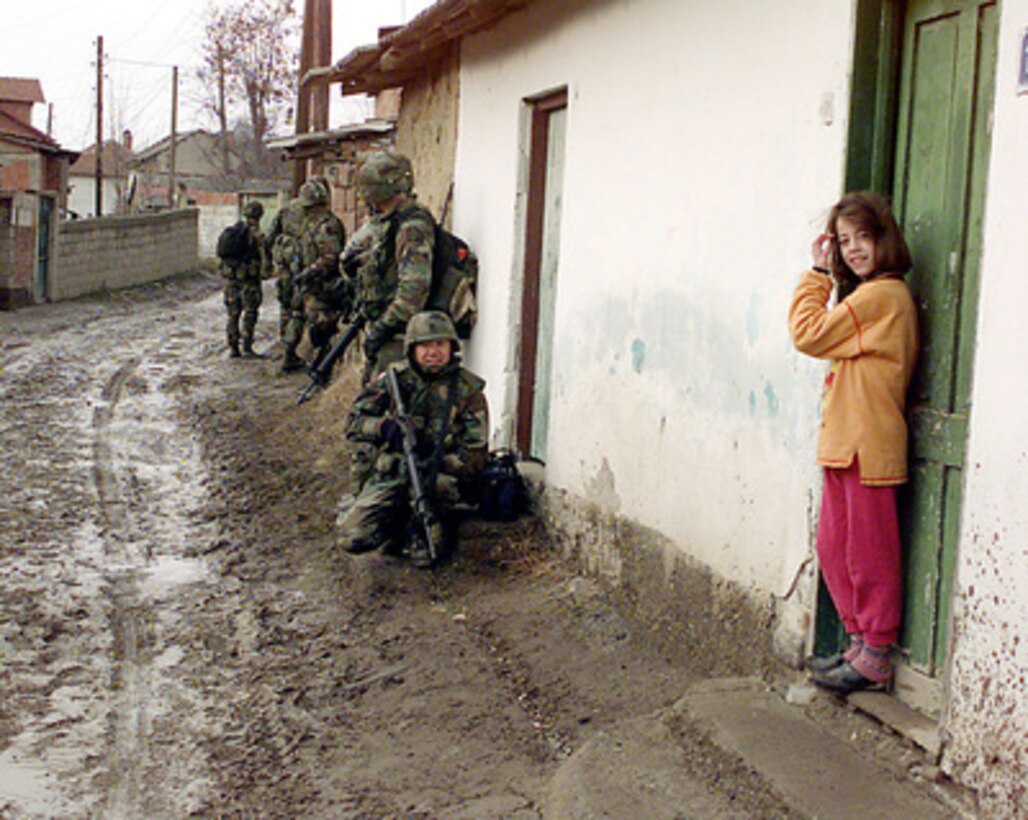 A young girl is amused to find U.S. Army soldiers lined up against the walls of her house in Mitrovica, Kosovo, on Feb. 21, 2000. The soldiers from the U.S. Army's Bravo Company, 3rd Battalion, 504th Parachute Infantry Regiment, and United Nations' police are conducting a house-to-house search for weapons. The soldiers are attached to the 82nd Airborne Division, Fort Bragg, N.C., and are deployed to Kosovo as part of KFOR. KFOR is the NATO-led, international military force in Kosovo on the peacekeeping mission known as Operation Joint Guardian. 