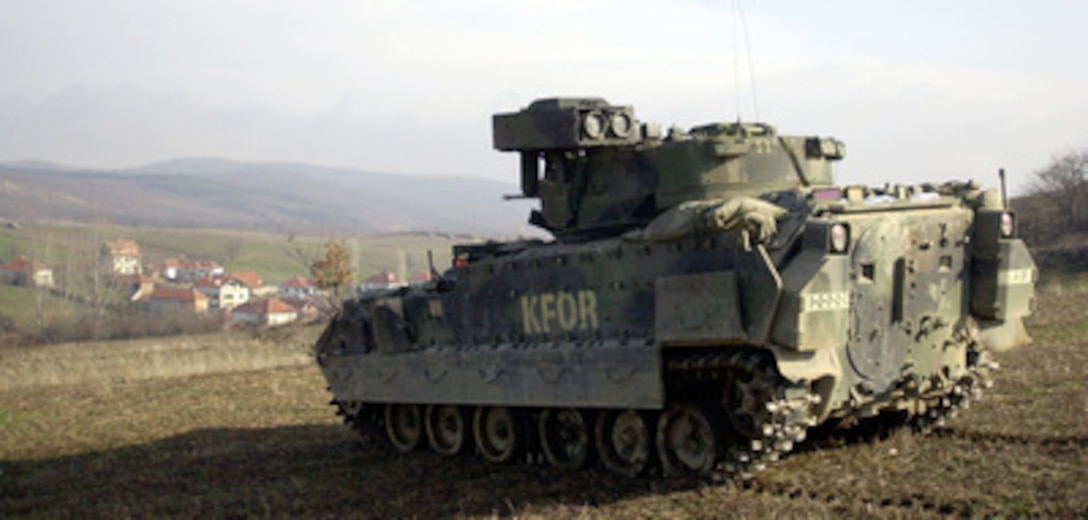 An M2 Bradley Fighting Vehicle stood guard over the village of Stublina as KFOR soldiers searched the houses below. KFOR soldiers carried out a carefully planned and orchestrated operation on Wednesday, March 15, 2000, to search and confiscate illegal weapons at five separate locations near the Serbian border. A total of 22 crates of ammunition, hand grenades, mines, rifles, other explosives, and chemical protective masks were found. KFOR is the NATO-led, international military force in Kosovo on the peacekeeping mission known as Operation Joint Guardian. 