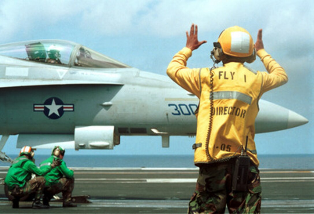 Petty Officer 3rd Class Michael DeForge (left) and Airman Brian Milless (center) check the hold-back bar on an F/A-18 Hornet while director Airman Edgar Centenorios (right) directs the pilot forward on the catapult before launching from the USS George Washington (CVN 73) on March 24, 2000. The aircraft carrier and her embarked aircraft are participating in a Composite Training Unit Exercise in the Gulf of Mexico. The three flight deck crewmen are Navy aviation boatswain's mates. 