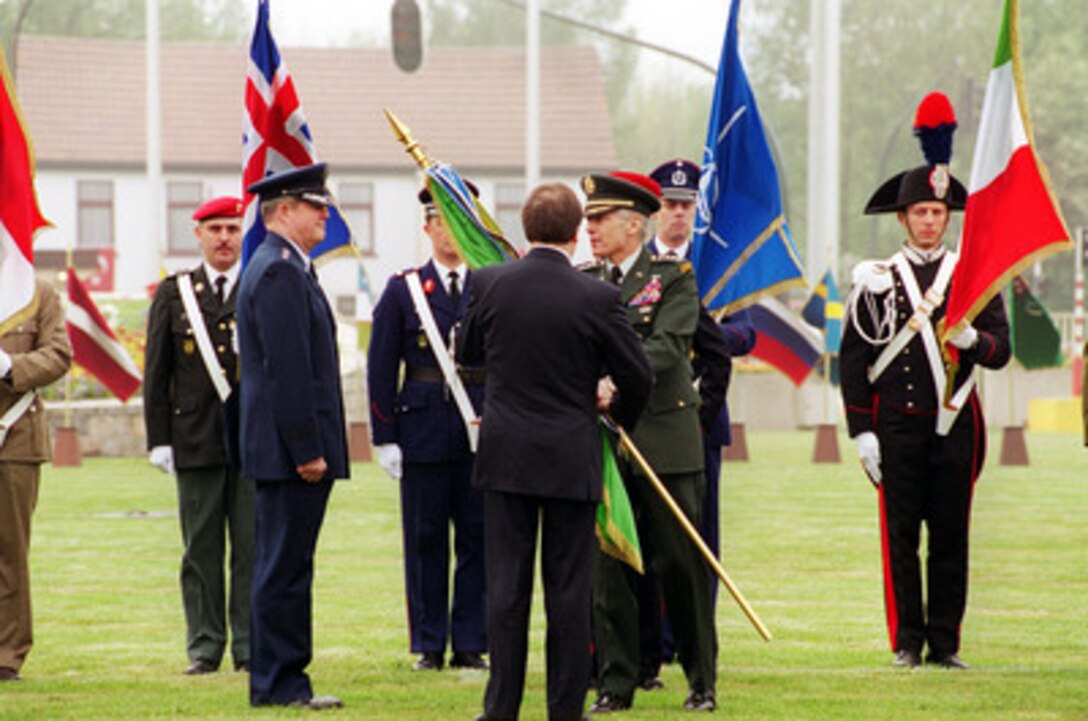 Outgoing Supreme Allied Commander Europe Gen. Wesley K. Clark (right) U.S. Army, passes the colors to NATO Secretary General Lord George Robertson (center) who will present them to the new commander Gen. Joseph W. Ralston (left), U.S. Air Force, at a change of command ceremony on May 3, 2000, at Supreme Headquarters Allied Powers Europe Headquarters, Mons, Belgium. 