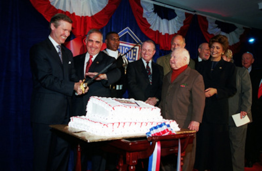 Secretary of Defense William S. Cohen (left) and retired Gen. John Tilelli, president of the United Service Organizations, prepare to cut a cake at a ceremony marking the opening of the USO Corridor in the Pentagon on Nov. 2, 2000. Cohen and Tilelli were joined on stage by Acting Assistant Secretary of Defense for Reserve Affairs Charles Cragin (3rd from left), actors Mickey Rooney (4th from left) and Gerald McRaney (behind Rooney) and Janet Langhart Cohen, wife of Secretary Cohen. The ceremony marked the opening of the display in the Pentagon commemorating the close relationship of the two organizations. 
