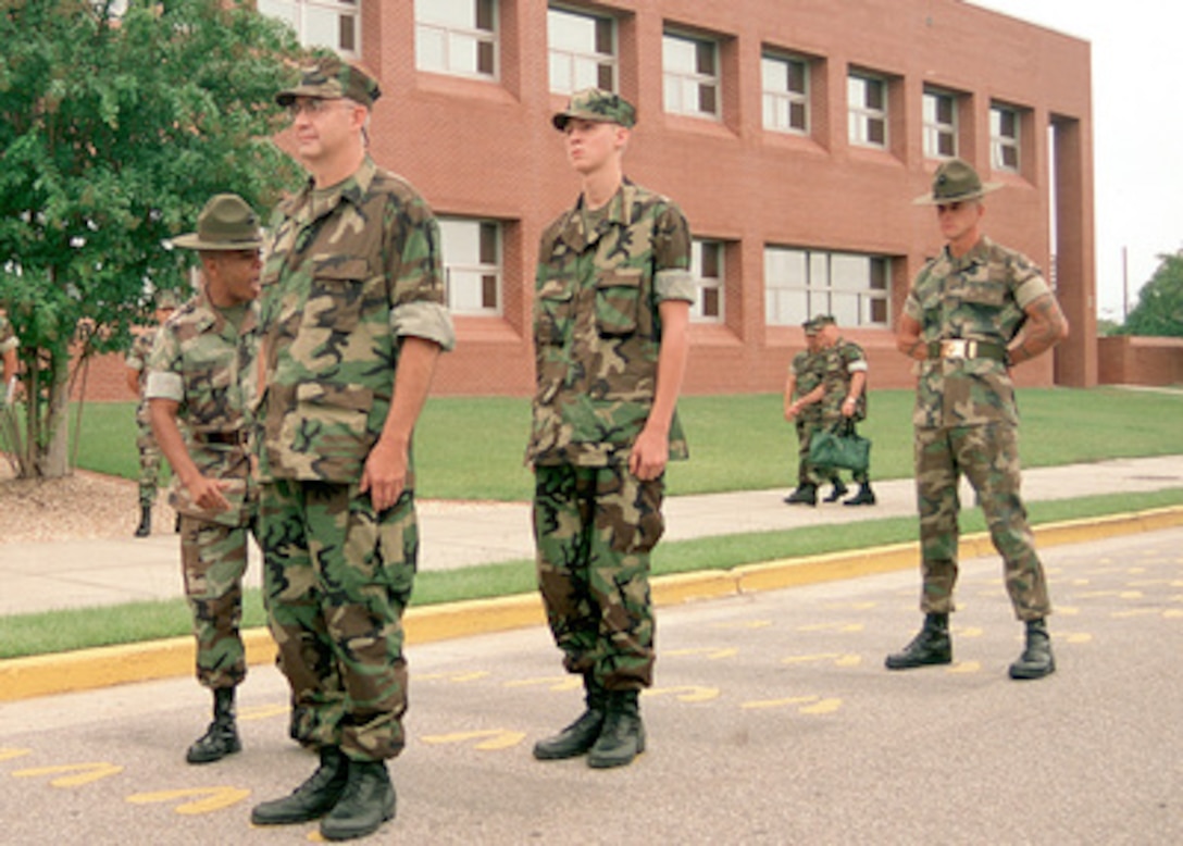 Senior Drill Instructor Sgt. Derrick Shuman (left) exhorts his latest recruits to keep their head and eyes forward during the yellow footprint orientation at Parris Island Recruit Training Depot, S.C., on Sept. 6, 2000. The two recruits are Richard A. Castanet and Christian Castanet, from Richmond Va. The elder Castanet is the Marine winner of the Yahoo! Fantasy Careers in Today's Military Contest. Father and son are experiencing Marine Corps training together. Drill Instructor Sgt. Lanny Powell (right) keeps an experienced eye on the new recruits. 