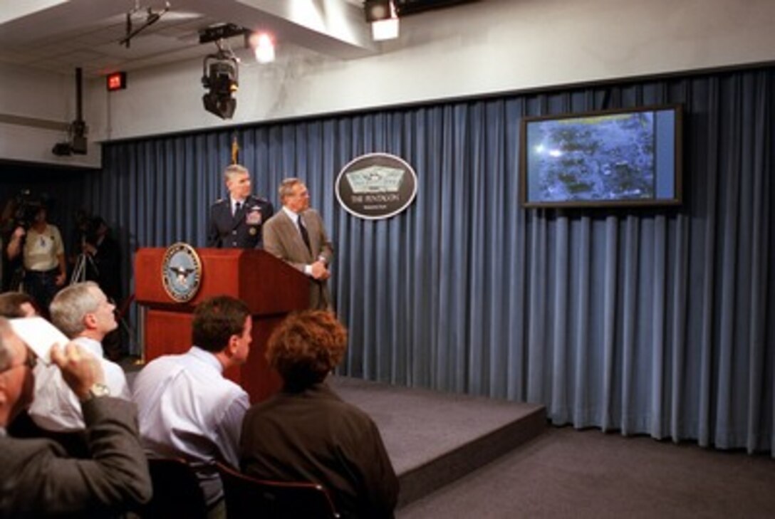 Secretary of Defense Donald H. Rumsfeld (right) watches the television screen as Chairman of the Joint Chiefs of Staff Gen. Richard B. Myers, U.S. Air Force, describes the area hit in an armament delivery recording shown during a Pentagon news briefing on Oct. 29, 2001. 