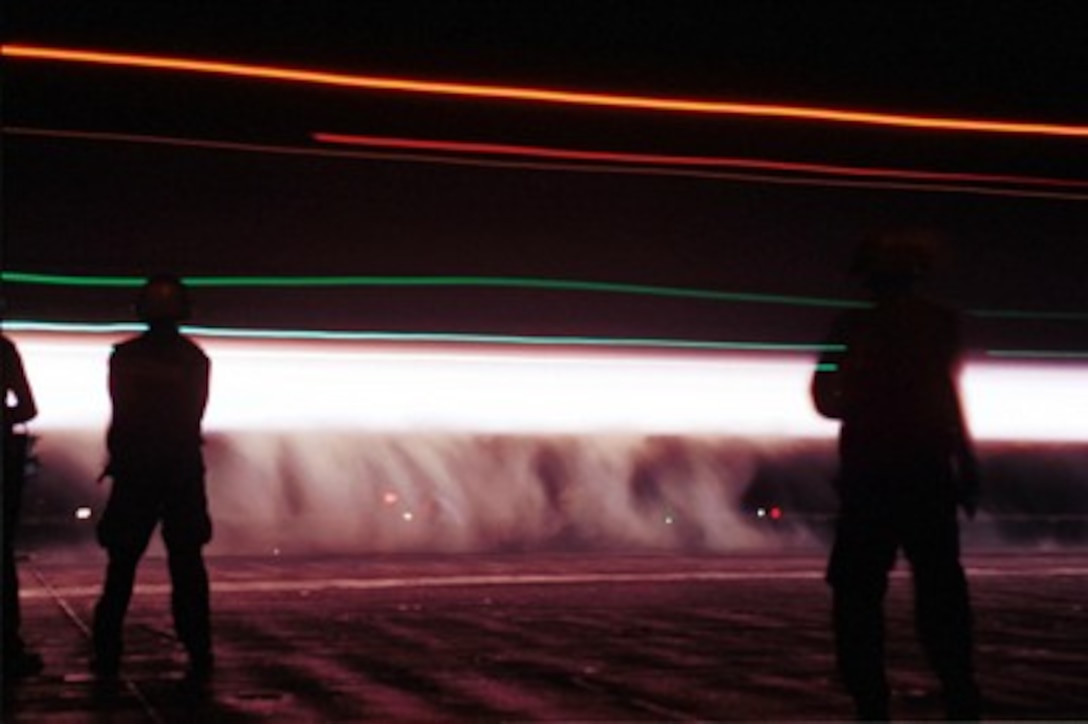 The night launch of a Navy F-14 Tomcat becomes a trail of steam and light silhouetting the flight deck crewmen on the USS Enterprise (CVN 65) on Oct. 7, 2001. The Enterprise is launching aircraft for strike missions against al Qaeda terrorist training camps and military installations of the Taliban regime in Afghanistan as part of Operation Enduring Freedom. The carefully targeted actions are designed to disrupt the use of Afghanistan as a base for terrorist operations and to attack the military capability of the Taliban regime. 