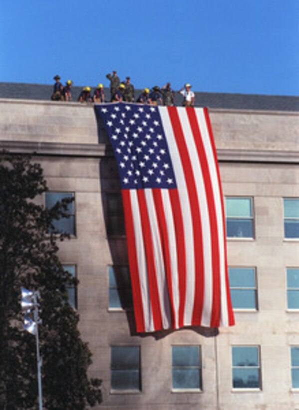 Fire fighters and military personnel unfurl a large American Flag from the roof of the Pentagon during the Sept. 12, 2001, visit of President George W. Bush to the site of the previous day's terrorist attack on the Pentagon. 