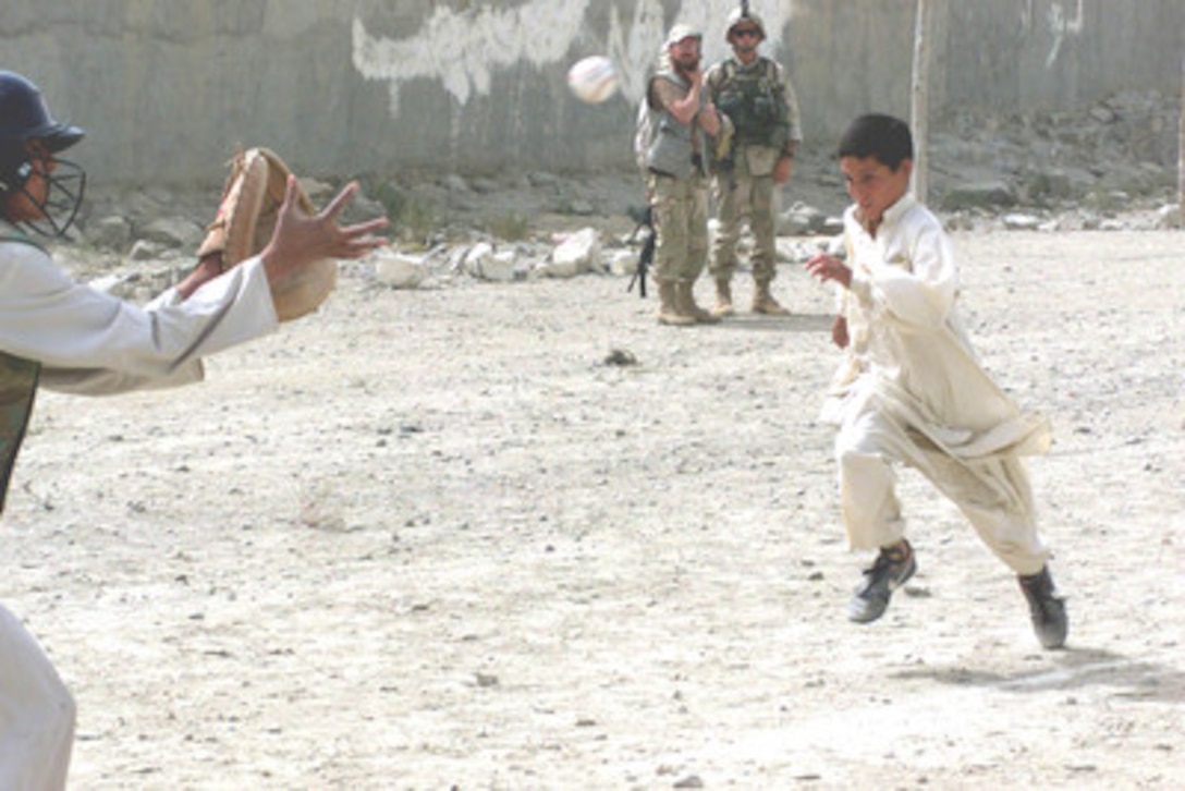 U.S. soldiers look on as the two teams of the Afghan little league square off in the fourth of their ten-game season. 