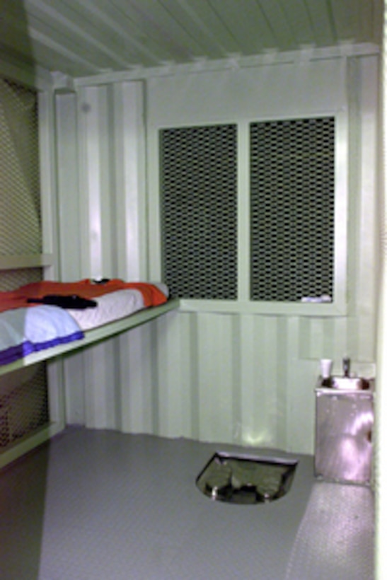 A detention unit at Camp Delta, Guantanamo Bay, Cuba, on December 3, 2002, showing bed, comfort items, toilet, and sink with potable water. 