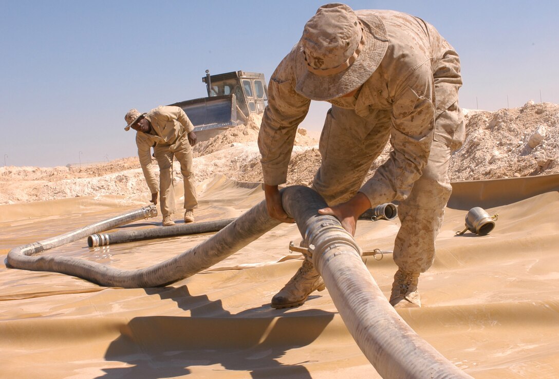 AL ASAD, Iraq (March 15, 2005) - While a bulldozer builds new lining walls, Lance Cpls. Gustaw D. Sasiadek (right), and Leon M. Jarvis, bulk fuel specialists with Combat Logistics Battalion 2, work to attach a fuel line to one of the fuel farm's 50,000 gallon bladders. The bulk fuel Marines of CLB-2 are redesigning the fuel farm to minimize damage from possible enemy rocket attacks.
