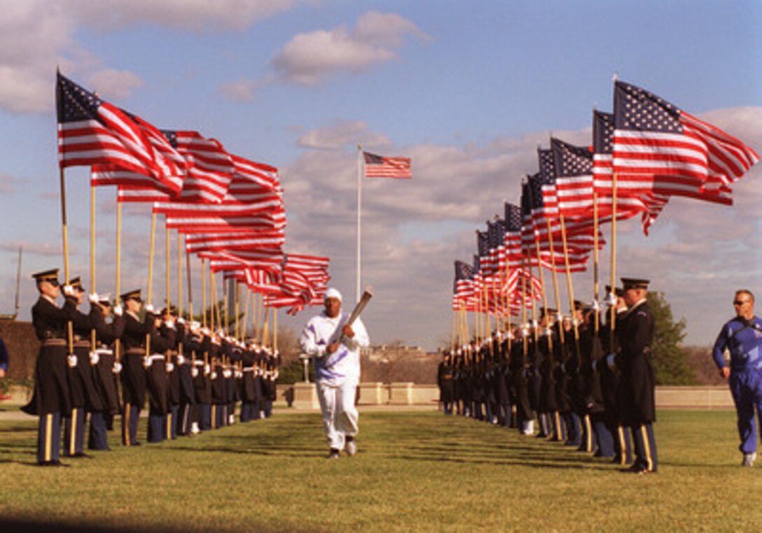 Navy Chief Petty Officer Bernard Brown carries the Olympic torch through a cordon of American flags on the Pentagon parade field at the start of the Dec. 21, 2001, ceremony. Sixteen persons directly affected by the Sept. 11, 2001, terrorist attack on the Pentagon were honored participants in the torch ceremony. The Olympic flame will continue on its way to Salt Lake City, Utah, where the Winter Games will begin on Feb. 8, 2002. 