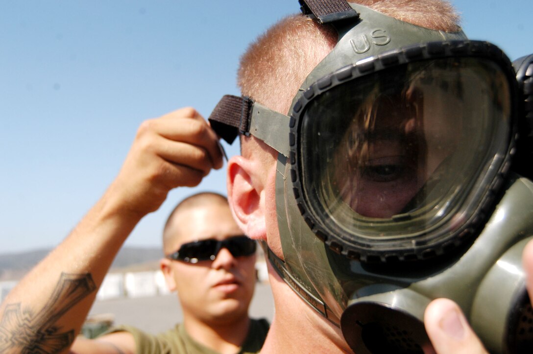Lance Cpl. Tom L. Belcher, an ammunition technician with Combat Service Support Group 15, 1st Force Service Support Group, tightens gas mask straps on Pfc. Galvin J. Murphy, also an ammo. tech., before he handles mortars emitting phosphine gas Aug. 17. Their ten-man crew was detoxifying the mortars to make them safe to use in Iraq. (Photo by Lance Cpl. Ray Lewis)