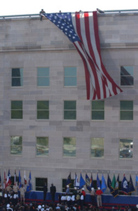 President George W. Bush and Secretary of Defense Donald H. Rumsfeld look up to see the flag of the United States draped over the side of the west wall during the Sept. 11 Observance Ceremony at the Pentagon. More than 13,000 people attended the service to remember those who lost their lives one year ago when terrorists crashed a commercial airliner into the Pentagon. 