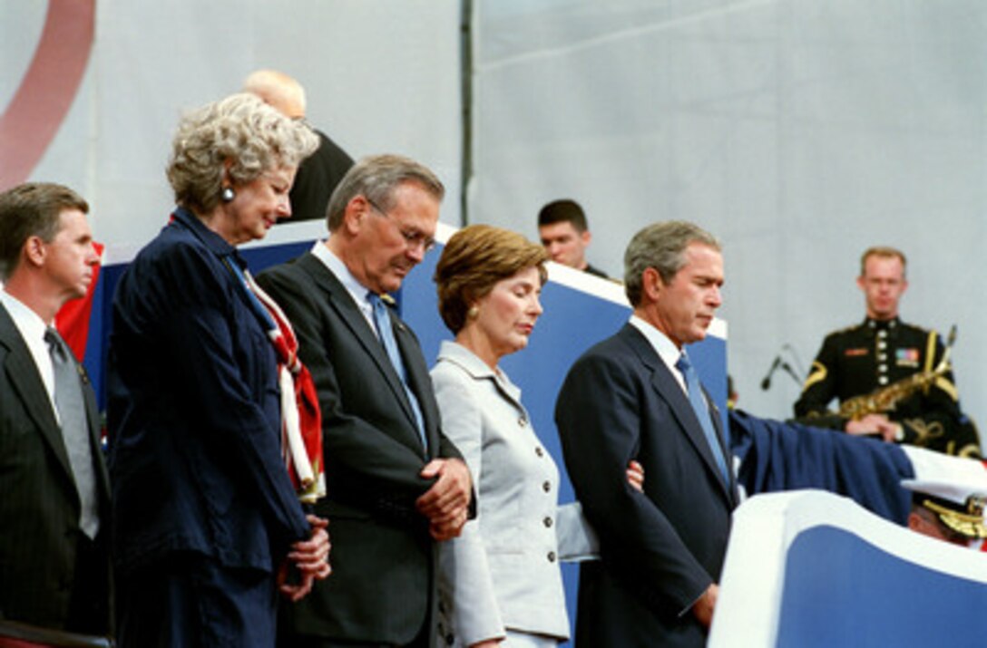 With their heads bowed during the invocation, the Rumsfelds and Bushes take part in the Sept. 11 Observance Ceremony at the Pentagon on Sept. 11, 2002. Bush and Rumsfeld joined more than 13,000 people at the service to remember those who lost their lives one year ago when terrorists crashed a commercial airliner into the Pentagon. The ceremony was held at the site of the terrorist attack, which was reconstructed within one year in what was known as the Phoenix Project. From left to right: Mrs. Joyce Rumsfeld, Secretary of Defense Donald H. Rumsfeld, First Lady Laura Bush, and President George W. Bush. 