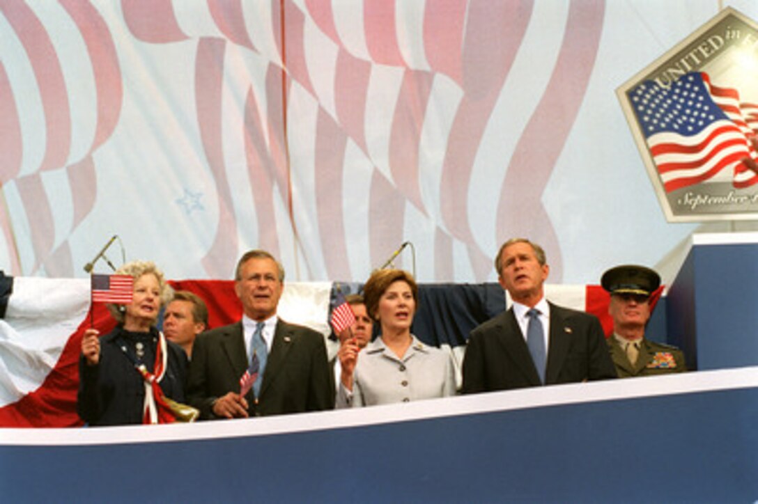 Mrs. Joyce Rumsfeld, Secretary of Defense Donald H. Rumsfeld, First Lady Laura Bush, President George W. Bush, and Commandant of the Marine Corps General James L. Jones, wave American flags as they take part in the Sept. 11 Observance Ceremony at the Pentagon on Sept. 11, 2002. They joined more than 13,000 people at the service to remember those who lost their lives one year ago when terrorists crashed a commercial airliner into the Pentagon. The ceremony was held at the site of the terrorist attack, which was reconstructed within one year in what was known as the Phoenix Project. 