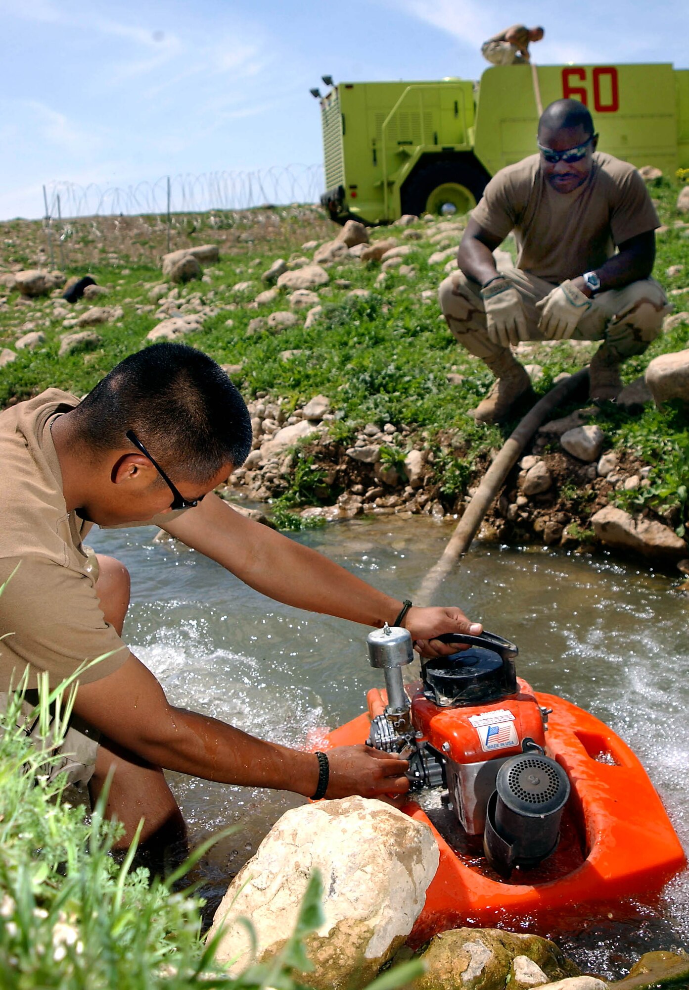 OPERATION IRAQI FREEDOM -- Airman 1st Class Brandon Olsen (left) and Senior Airman Dwight Moses pump water  from a stream near Bashur Airfield, Iraq, to fill their P-19 fire truck.  The firefighters are from a host of bases, but attached to the 86th Expeditionary Contingency Response Group.  They make several trips a week to the stream to get water for the airfield.  (U.S. Air Force photo by Master Sgt. Keith Reed) 