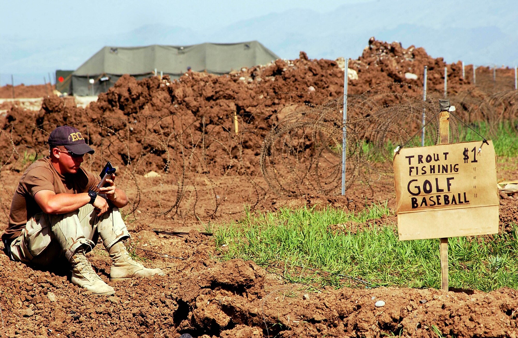 OPERATION IRAQI FREEDOM -- Senior Airman Ian Garcia takes a break at Bashur Airfield in northern Iraq.  Garcia is part of a six-man explosive ordnance disposal team at the base.  He said he put up the sign next to a mud hole because he was tired of seeing people walk by frowning, and he wanted them to smile.  Garcia is deployed from Nellis Air Force Base, Nev.  (U.S. Air Force photo by Master Sgt. Keith Reed)