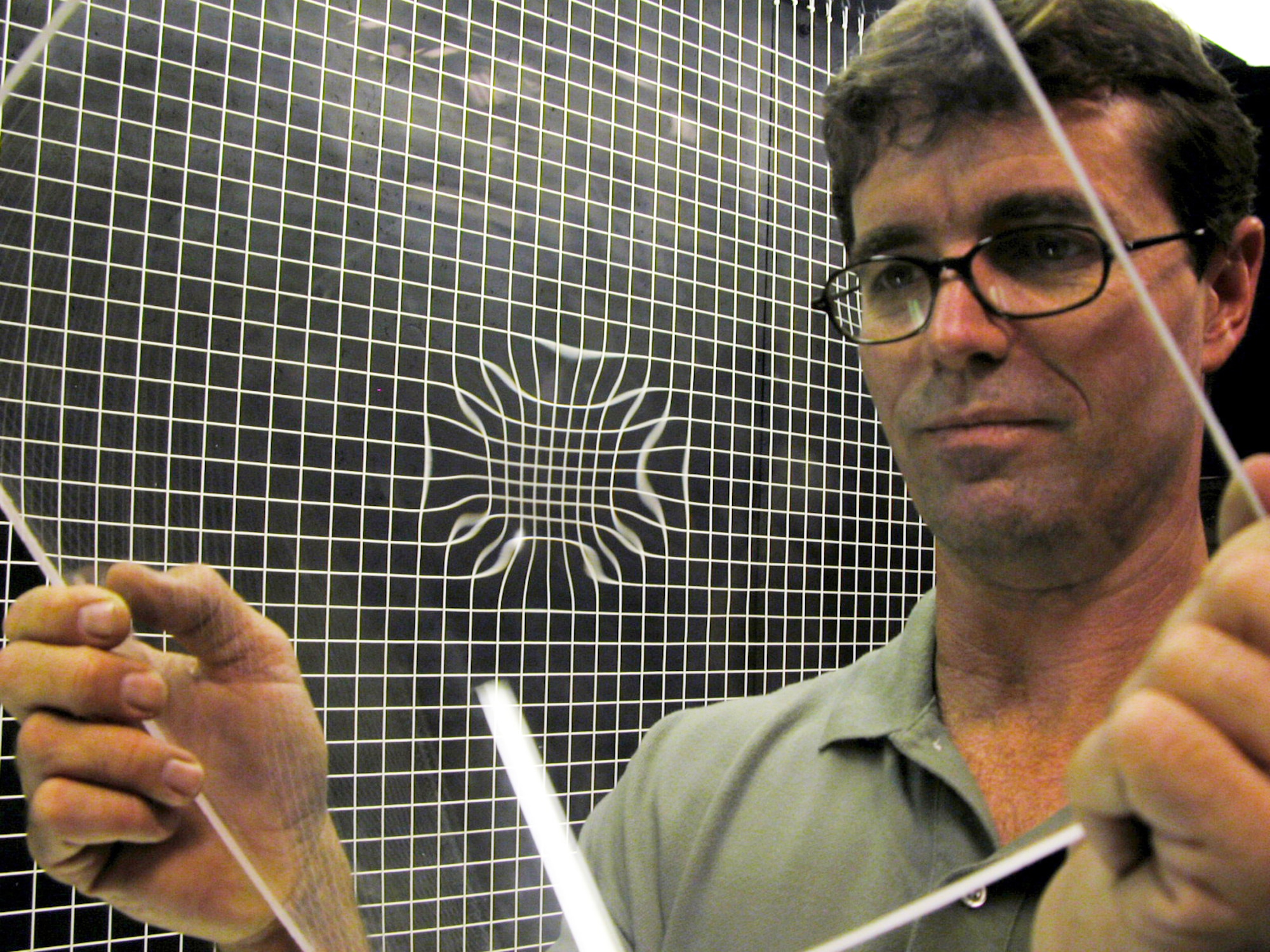 ROBINS AIR FORCE BASE, Ga. -- Peter Wellman holds a piece of F-15 canopy in front of a grid board that shows a distortion from an improper field repair.  Imperfections like these have to be fixed to give pilots an unobstructed view.  (U.S. Air Force photo by Sue Sapp)