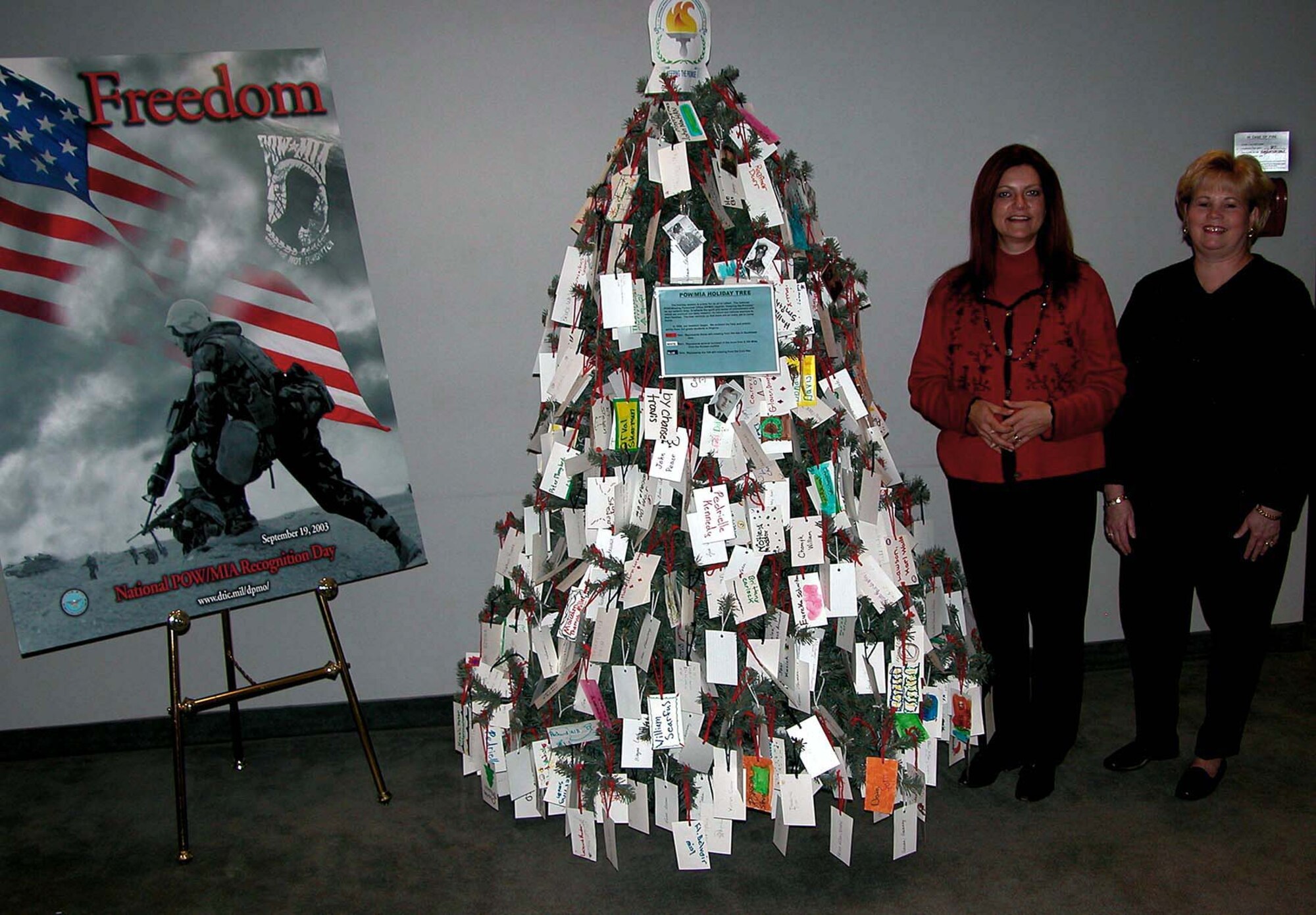 WASHINGTON -- Retired Army Master Sgt. Peggy Marish-Boos (left) and Debbie Landon pose by the POW/MIA holiday tree they decorated it as a reminder to people in the Defense POW/Missing Personnel Office of why they do what they do.  At the left is the 2003 National POW/MIA Recognition Day poster.  (Department of Defense photo by Rudi Williams)
