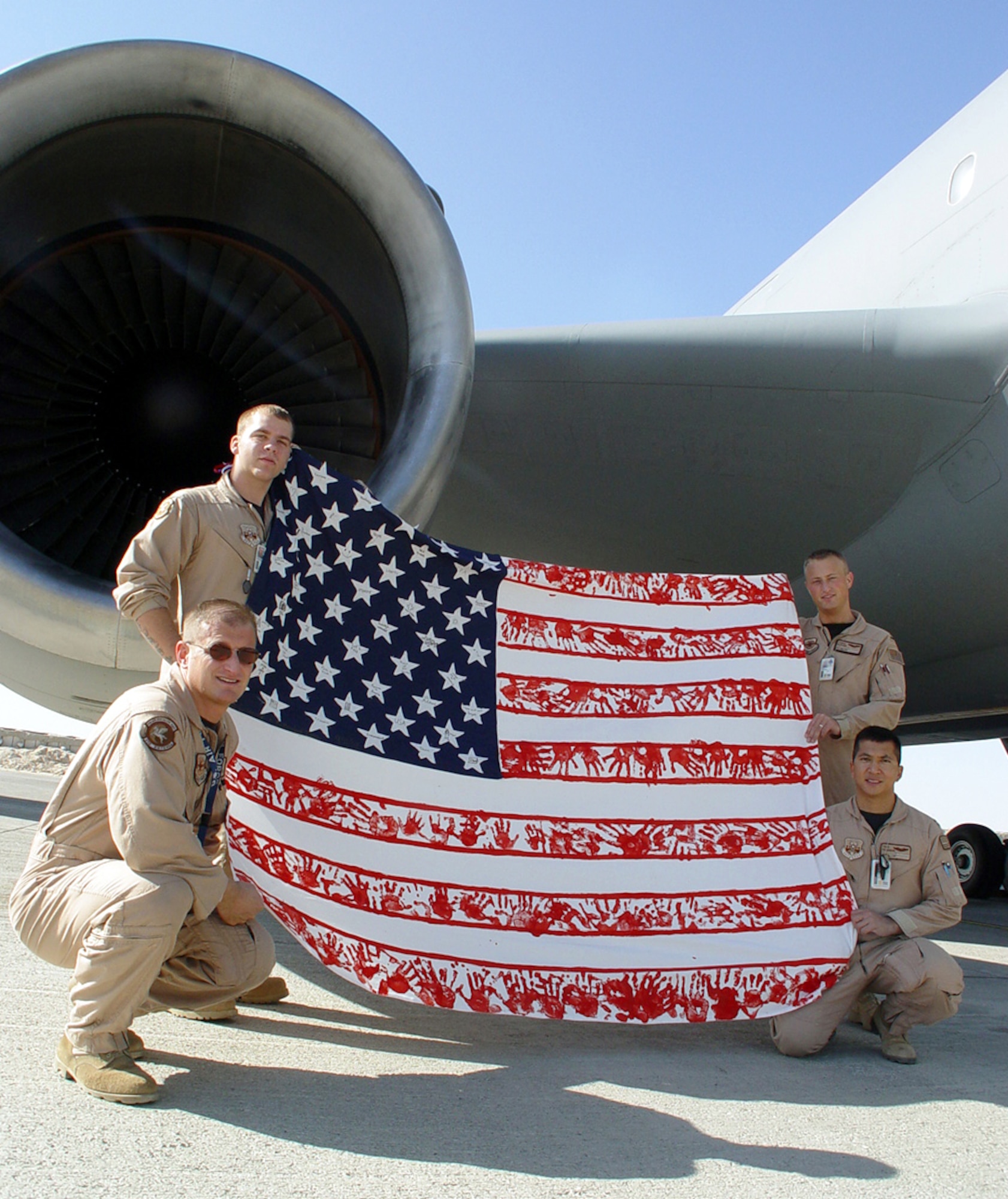 OPERATION ENDURING FREEDOM -- (Clockwise from left) Staff Sgt. C.D. Schmeid, Airman 1st Class Dustin Sharpmack, 1st Lt. Trace Dotson and Capt. Troy Panon display an 86-by-76-inch handmade American Flag.  The one-of-a-kind flag was designed and created by Iowa school students as part of the "Hand on America" project.  The crew displayed the flag on a flight over Iraq on Dec. 9.  The airmen are all part of a KC-10 Extender crew who are at a forward-deployed location.  (U.S. Air Force photo by Airman 1st Class Brandi Branch)