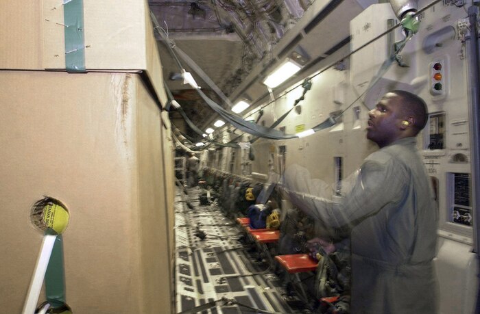 OPERATION ENDURING FREEDOM -- A U.S. Air Force loadmaster identified only as "Chris" removes tie-down straps from TRIADS prior to reaching the drop zone. U.S. Air Force crew members from Charleston Air Force Base, S.C., continue high altitude drops of HDRs (Humanitarian Daily Rations) from their C-17 Globemaster III somewhere over northern Afghanistan, Oct. 18. The C-17 dropped 42 TRIADS containing 17,220 HDRs. Approximately 500,000 HDRs have been dropped into Afghanistan since the humanitarian relief effort began. (U.S. Air Force photo by Mannie Garcia/Gannett/ATPCo)