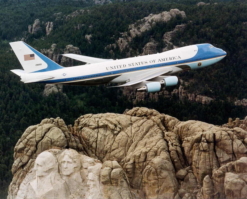 FILE PHOTO -- Air Force One flies over Mount Rushmore. Principal differences between the VC-25A and the standard Boeing 747, other than the number of passengers carried, are the electronic and communications equipment aboard Air Force One, its interior configuration and furnishings, self-contained baggage loader, front and aft air-stairs, and the capability for in-flight refueling. These aircraft are flown by the presidential aircrew, maintained by the presidential maintenance branch, and are assigned to Air Mobility Command's 89th Airlift Wing, Andrews Air Force Base, Md. (U.S. Air Force photo)