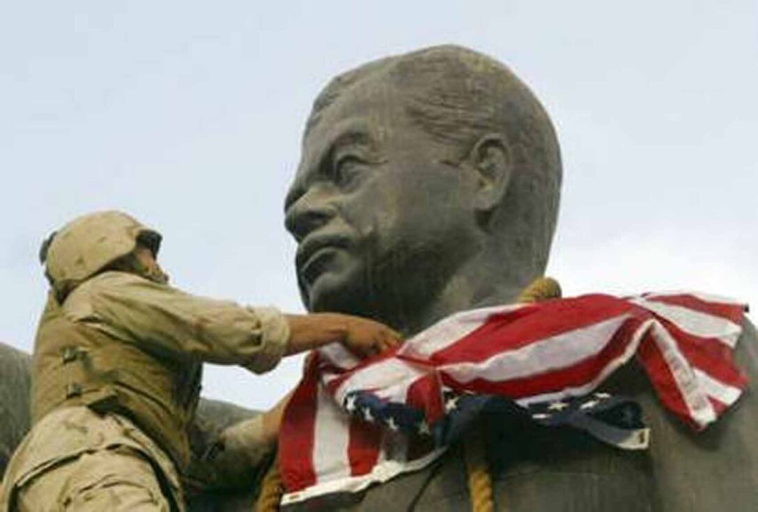 Former Cpl. Edward Chin places the U.S. Flag over a statue of Saddam signifing the liberation of the Iraqi people in 2003 during Operation Iraqi Freedom.