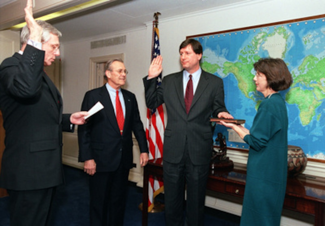 Deputy Under Secretary of Defense for Installations & Environment Raymond DuBois (left) administers the oath of office to Stephen Cambone (center) as the new Under Secretary of Defense for Intelligence during a ceremony in the Pentagon office of Secretary of Defense Donald H. Rumsfeld (2nd from left) on March 11, 2003, while Cambone's wife, Margaret, holds the Bible. Rumsfeld created the position to emphasize the importance of intelligence gathering and interpretation in the new security environment of the 21st century. 