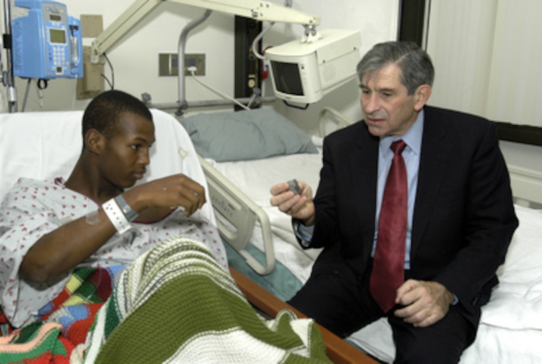 Army Pfc. Michael Wright shows Deputy Secretary of Defense Paul Wolfowitz the piece of shrapnel doctors removed from his knee after the humvee he was riding in hit a land mine. Wolfowitz stopped by Walter Reed Army Medical Center in Washington, D.C., on Nov. 11, 2003, to visit with some of the wounded soldiers recovering there before joining President Bush at Arlington National Cemetery for the traditional Veterans Day observances. Wright was serving in Iraq with the 501st Parachute Infantry Regiment of the 82nd Airborne Division when he was wounded. He told Wolfowitz that he hopes to be able to rejoin his unit and even make parachute jumps with them. 