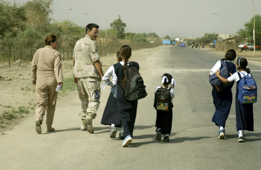 FRENCH VILLAGE, Iraq -- Senior Master Sgt. Tommie Tracey (left) and Maj. (Dr.) Gene Delaune stroll the streets here with local children.  Tracey is deployed with the Indiana Air National Guard's 122nd Fighter Wing.  Delaune is an individual mobilization augmentee deployed from the 89th Medical Group at Andrews Air Force Base, Md.  (U.S. Air Force photo by Master Sgt. Keith Reed)