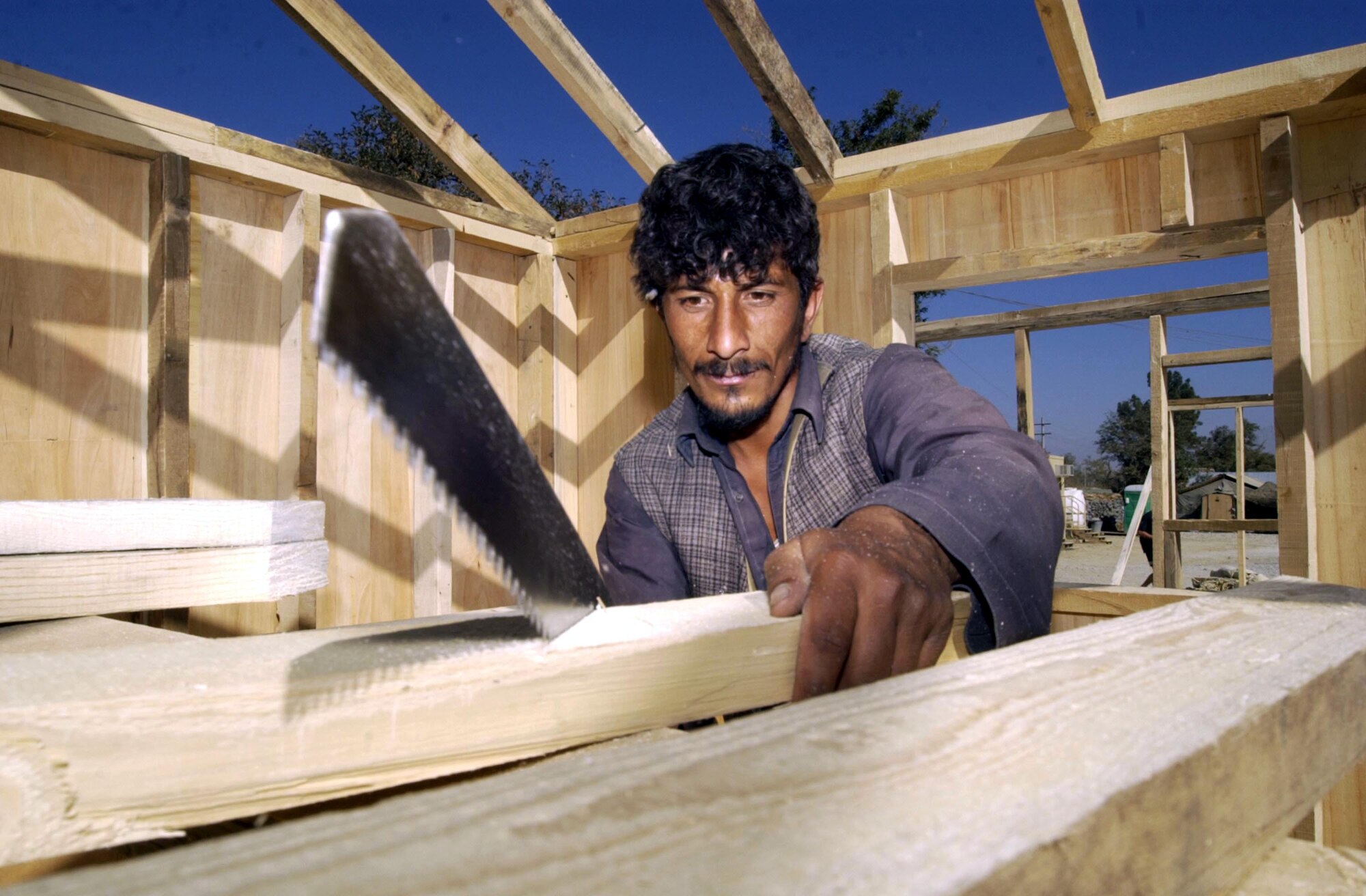 BAGRAM AIR BASE, Afghanistan -- Fazell uses a hand saw to cut a plank inside a B-hut at Air Force Village here.  Afghan carpenters construct these huts using only hand tools.  Even sheets of plywood are cut by hand.  The huts will replace the temper tents as living quarters.  (U.S. Air Force photo by Staff Sgt. Russell Wicke)