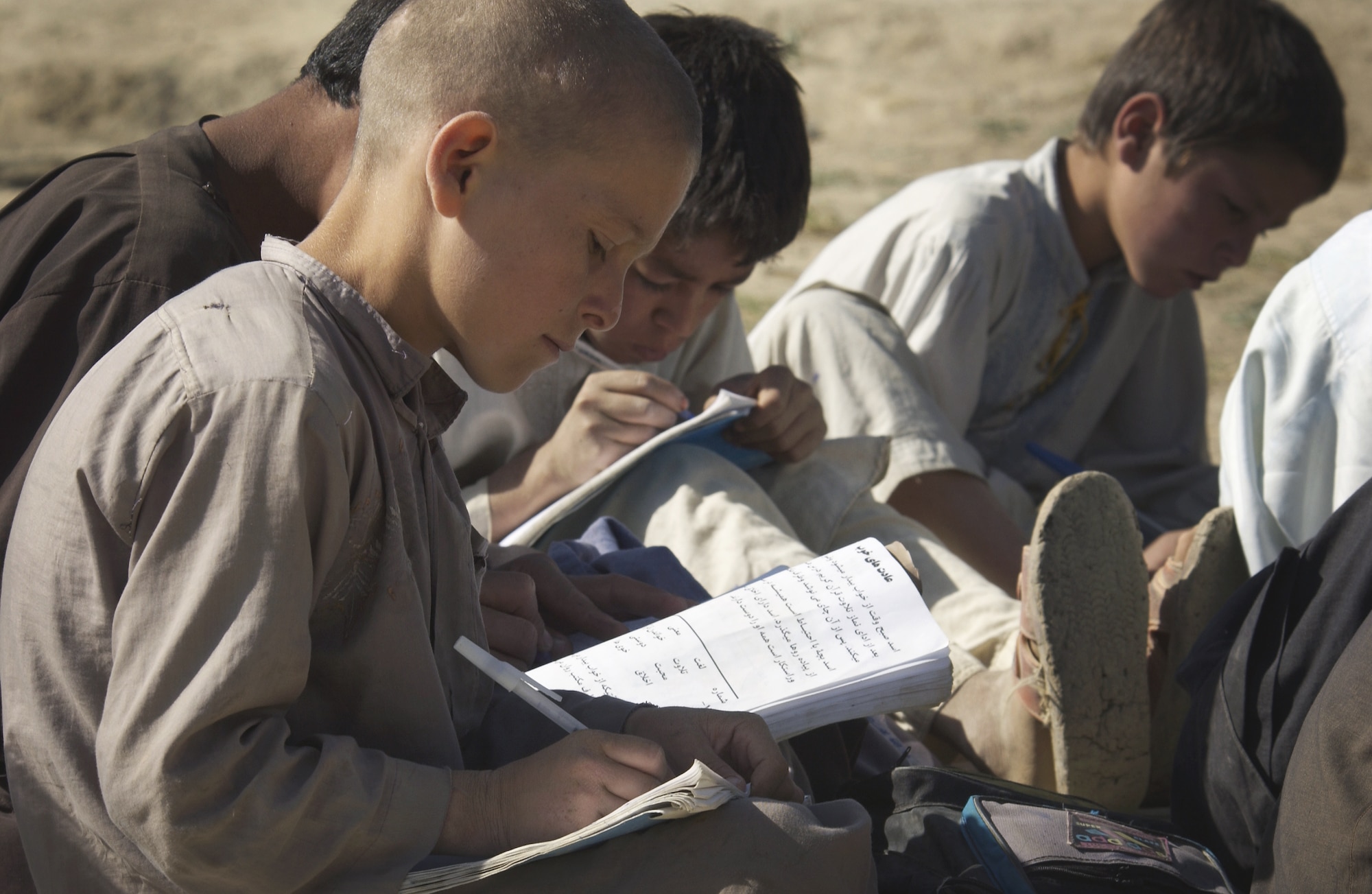 BAGRAM, Afghanistan -- Afghan boys study writing at an outdoor school.  Whenever the winds blow, or it rains, school is cancelled.  On Oct. 19, airmen delivered an old eight-section tent that will serve as a new school for the children.  (U.S. Air Force photo by Master Sgt. Lance Cheung)