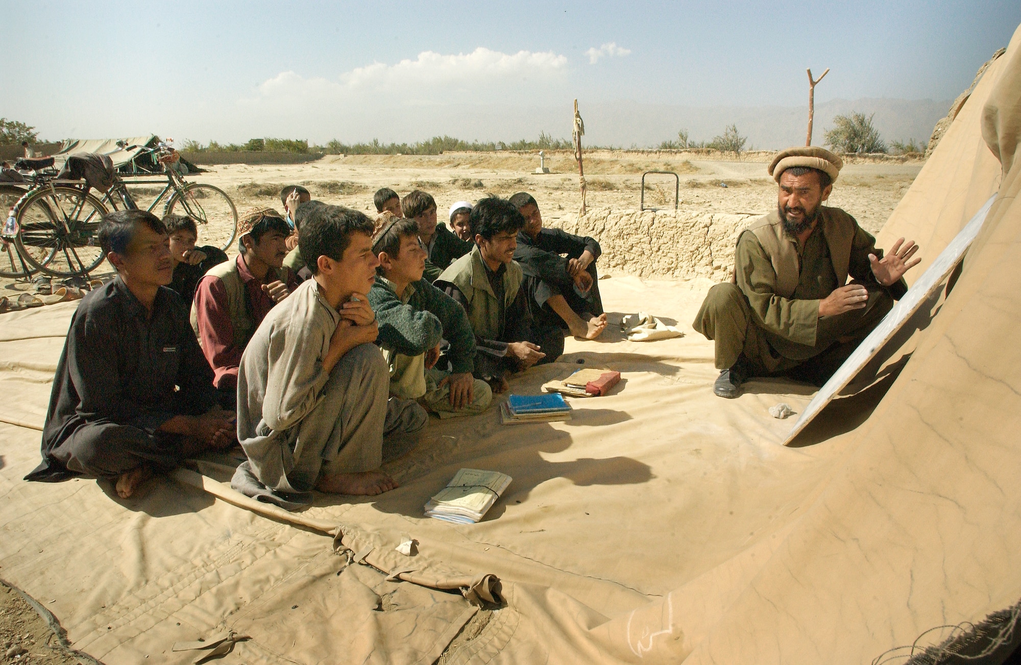 BAGRAM, Afghanistan -- A math teacher props his board against a mud wall to teach older Afghan boys.  Whenever the winds blow, or it rains, school is cancelled.  On Oct. 19, airmen delivered an old eight-section tent that will serve as a new school for the children.  (U.S. Air Force photo by Master Sgt. Lance Cheung)