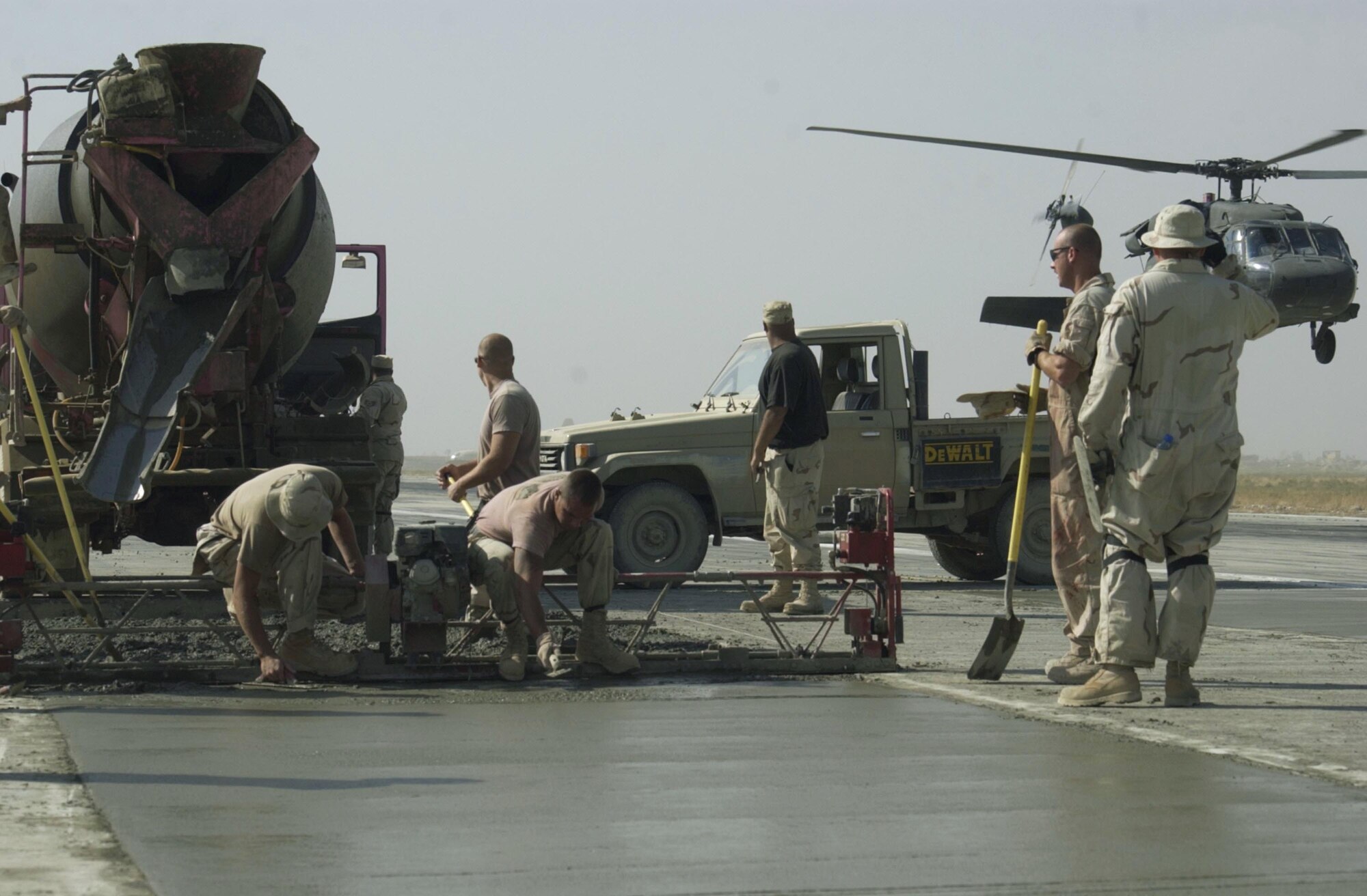 BAGRAM AIR BASE, Afghanistan -- Airmen of the 455th Civil Engineer Flight work together to pour the last load of concrete for the runway here as a Blackhawk helicopter flies by on the other half of the runway.  (U.S. Air Force photo by Staff Sgt. Russell Wicke)