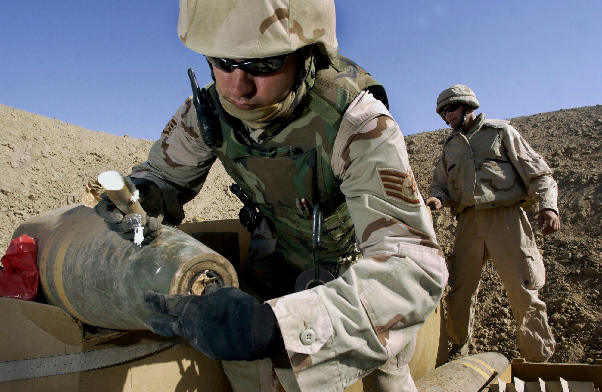 KIRKUK AIR BASE, Iraq -- Staff Sgt. Doug Baker (foreground) and Latvian navy Warrant Officer Guntars Jeromans prepare to destroy more than 180 120 mm mortar rounds.  Baker carefully loads PE-4, a British plastic explosive, into a 1,000-pound "dumb bomb" to detonate the load of more than 10,000 pounds of recovered Iraqi ordinance.  Baker and Jeromans are both assigned to the 506th Expeditionary Civil Engineer Squadron's explosive ordnance disposal flight here.  (U.S. Air Force photo by Master Sgt. Keith Reed)