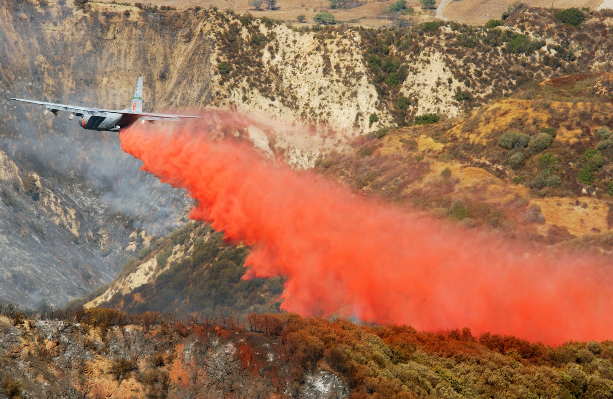 SOUTHERN CALIFORNIA -- A  C-130E Hercules Modular Airborne Fire Fighting System from the 146th Airlift Wing at Channel Islands Air National Guard Station, Calif.,  makes a Phoschek fire retardant drop on the Simi fire here Oct. 28. Pilots flying eight Air Force C-130 Hercules cargo airplanes have dropped 129,600 gallons of retardant on the Simi fire during 48 sorties and 32 flying hours as of Oct. 29.  (U.S. Air Force photo by Senior Master Sgt. Dennis W. Goff)