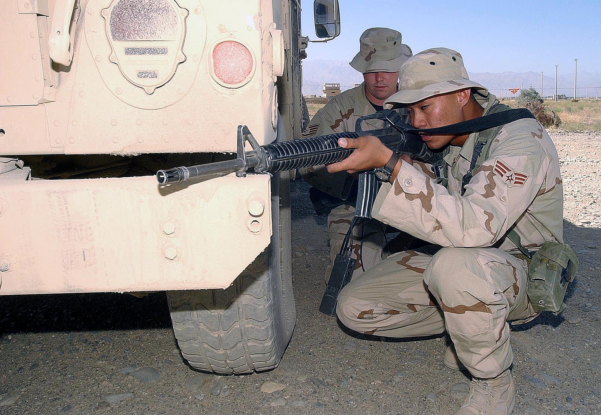 BAGRAM AIR BASE, Afghanistan -- Senior Airman Zane Aguilar (right) practices a defensive posture behind an armored Humvee as Staff Sgt. Alan Clontz calls in on the radio.  The airmen are assigned to the 455th Expeditionary Security Forces Squadron here.  Hostile encounters are likely on the perimeter of the base here.  Air Force security forces work with the Army to secure the base.  (U.S. Air Force photo by Staff Sgt. Russell Wicke)