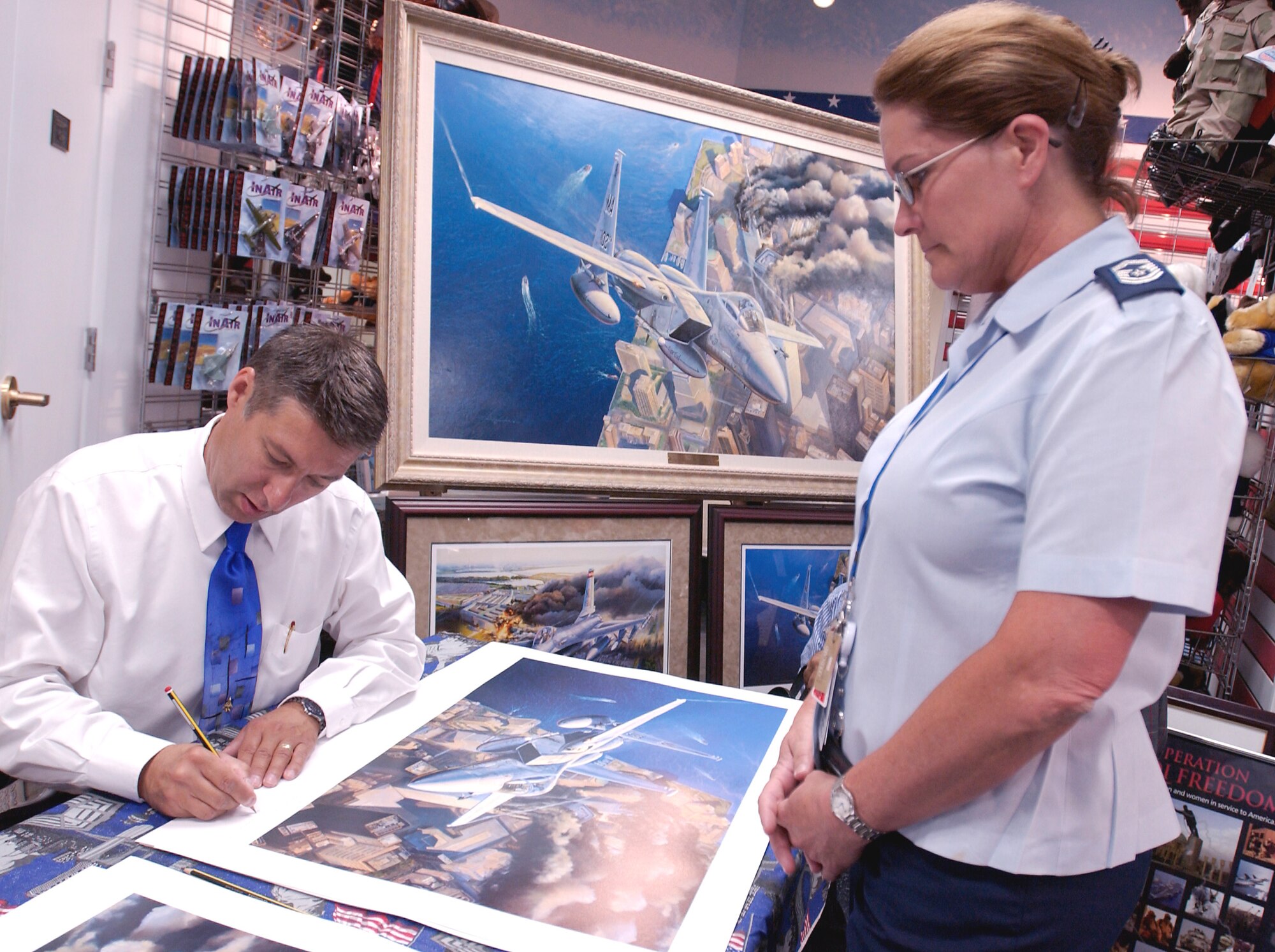 WASHINGTON -- Senior Master Sgt. Karla Taylor (right) watches artist Rick Herter sign a print of his original oil painting "Ground Zero, Eagles on Station" during an autograph session in the Pentagon on Sept. 9.  The artist also signed copies of  "First Pass, Defenders over Washington."  Profits from the sale of the prints will go to the Pentagon Memorial Fund.  (U.S. Air Force photo by Master Sgt. Jim Varhegyi)