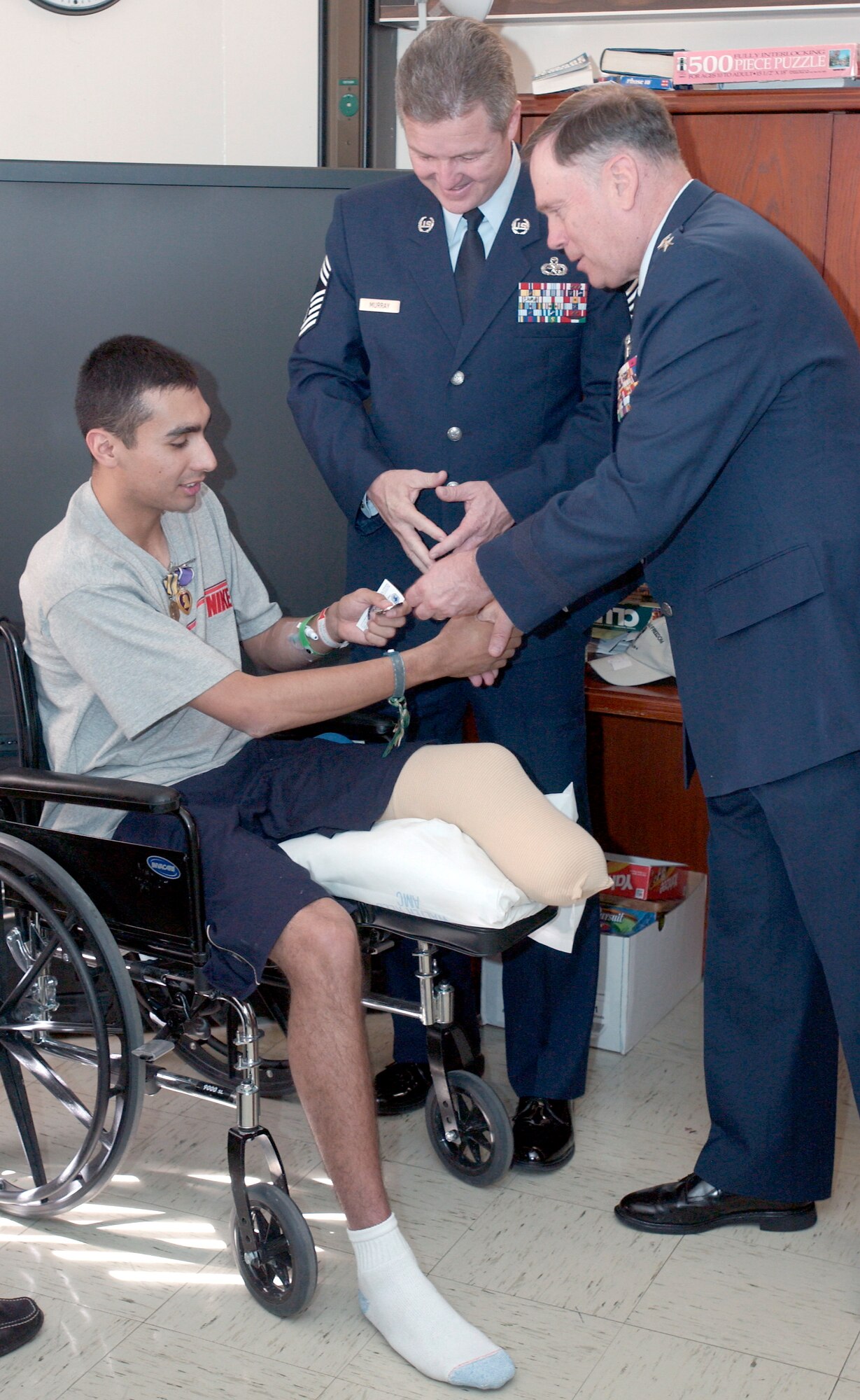 WASHINGTON -- Chief Master Sgt. of the Air Force Gerald R. Murray (center) watches Air Force Chief of Staff Gen. John P. Jumper present his coin to Airman 1st Class Scott Palomino.  General Jumper also presented him with a Purple Heart and an Air Force Commendation Medal at Walter Reed Army Medical Center on April 20.  Airman Palomino is a surveillance technician from the 603rd Air Control Squadron based at Aviano Air Base, Italy.  He was wounded April 10 when a mortar round exploded in his tent at Balad AB, Iraq.  As a result of the wound, Airman Palomino's leg had to be amputated below the knee.  (U.S. Air Force photo by Master Sgt. Jim Varhegyi)