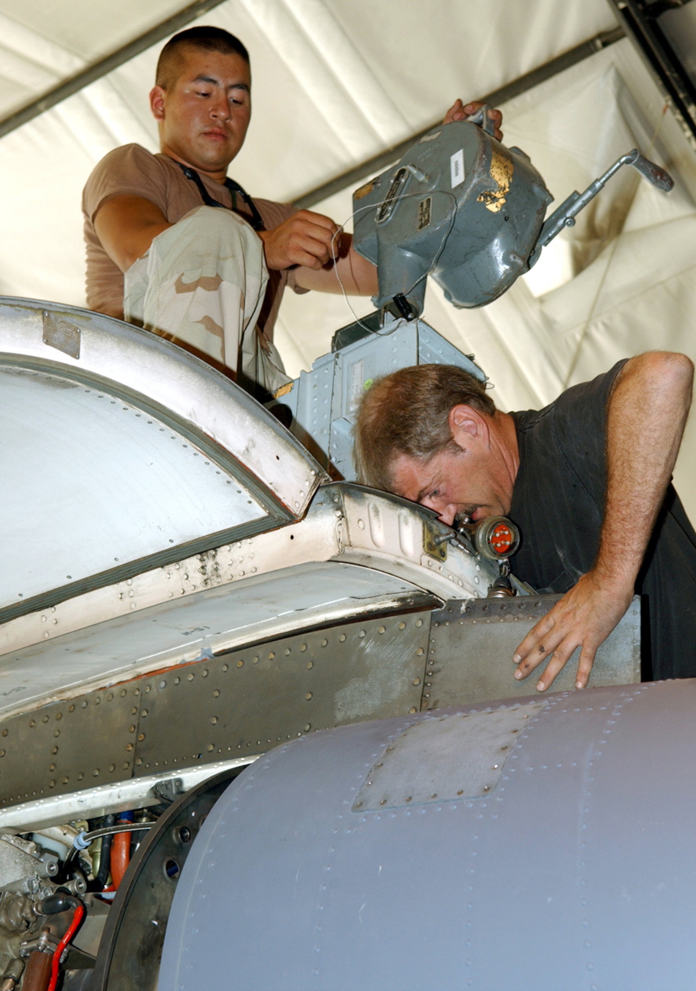 BAGRAM AIR BASE, Afghanistan -- Senior Airman Christopher Dalbec (top) cranks a hoist while Tom Ross connects cables to an engine during an engine swap.  Both men are deployed as part of the 354th Expeditionary Aircraft Maintenance Squadron.  (U.S. Air Force photo by Master Sgt. Andrew Gates)