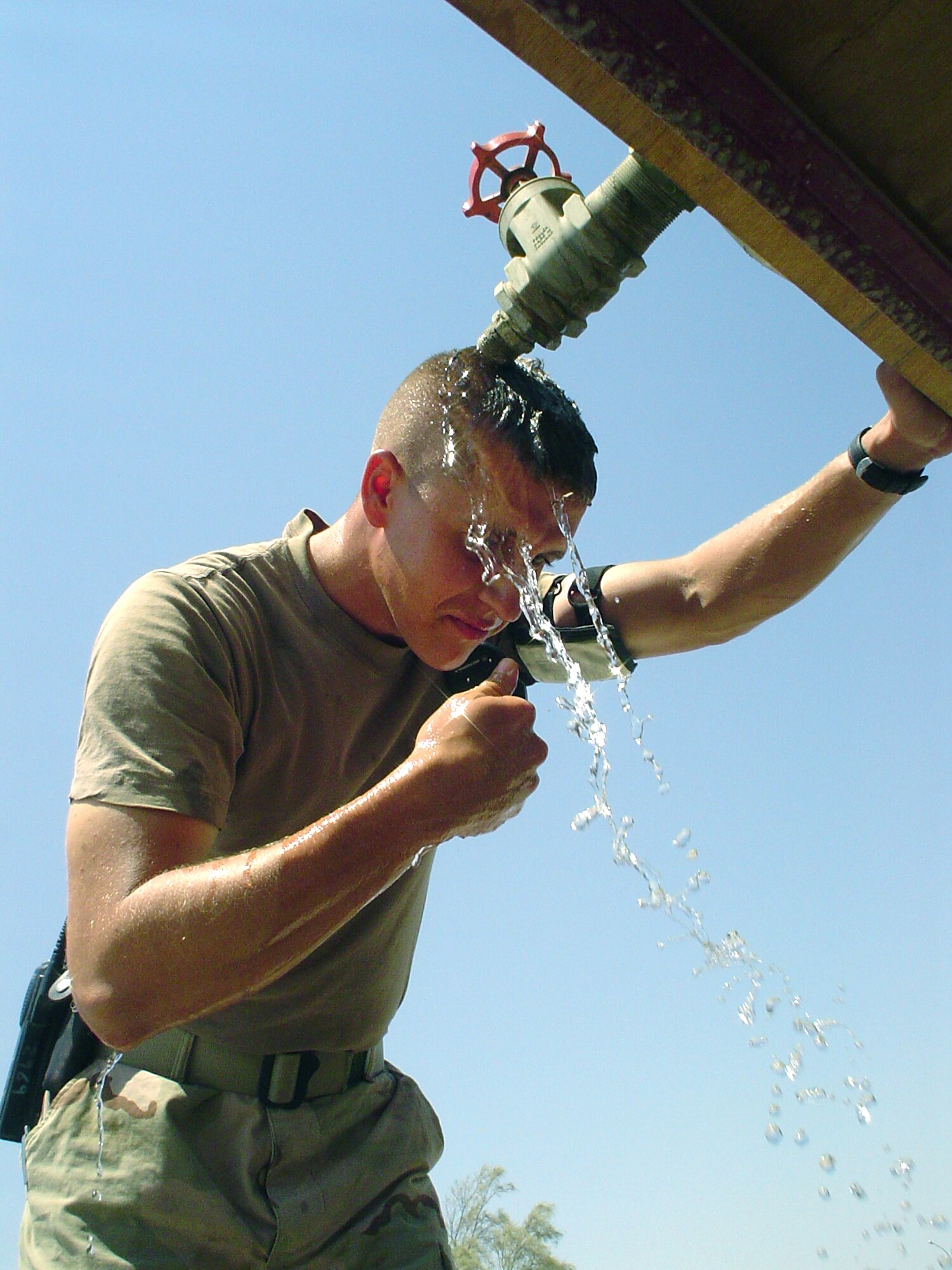 TALLIL AIR BASE, Iraq -- Staff Sgt. Jeremy Riggleman rinses away the heat of the day under a water buffalo here.  He is a power-production craftsman with the 407th Expeditionary Civil Engineer Squadron.  With temperatures routinely topping 120 degrees, heat is one of the biggest enemies warfighters face here.  (U.S. Air Force photo by Master Sgt. Debbie Aragon)