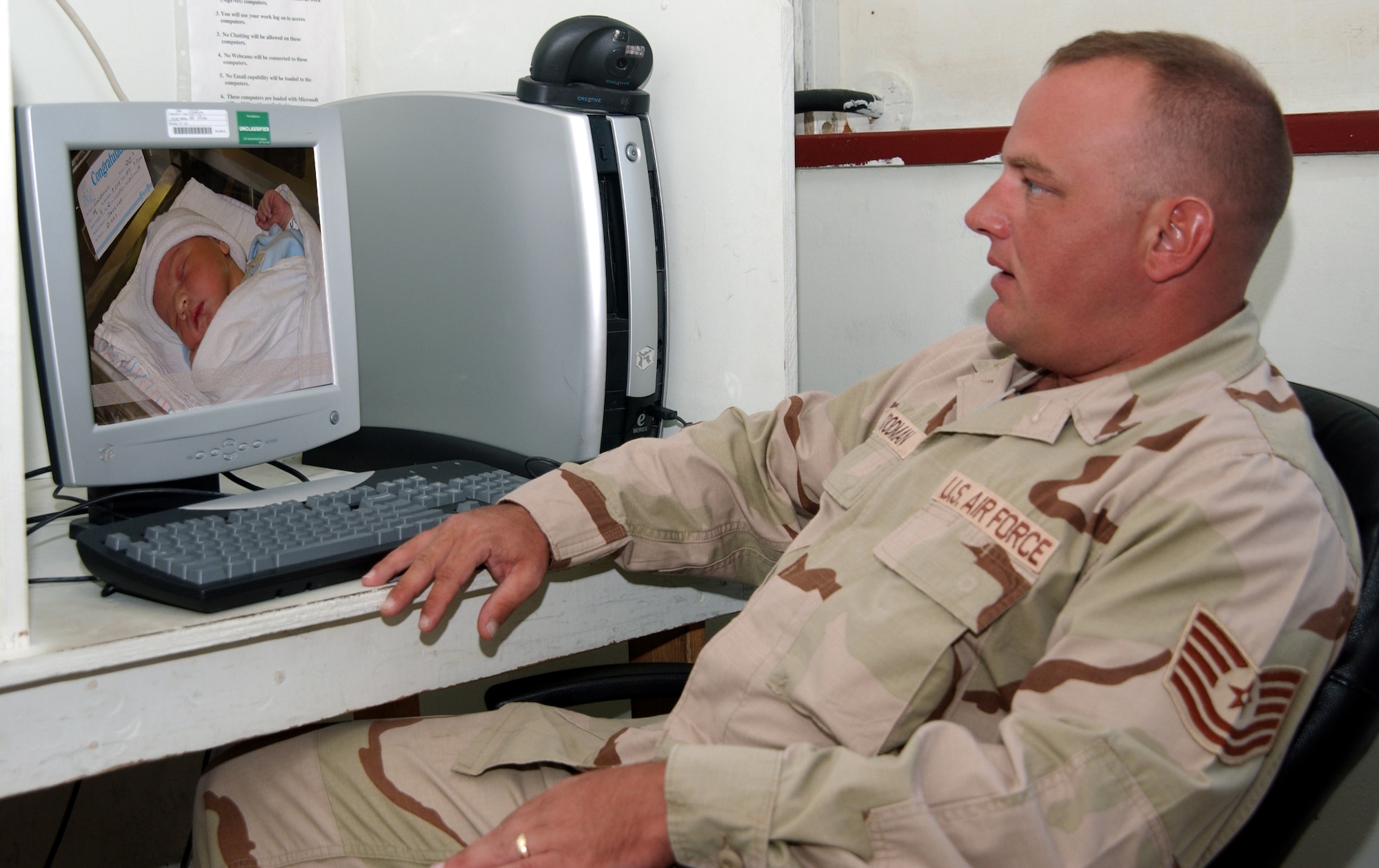 OPERATION ENDURING FREEDOM -- Tech. Sgt. Troy Goodman inspects the newest member of his family via Webcam Aug. 12.  Sergeant Goodman was able to watch the live birth over the Internet.  He is the noncommissioned officer in charge of munitions inspections for the 40th Expeditionary Munitions Flight.  (U.S. Air Force graphic by Master Sgt. Sean Brennan)