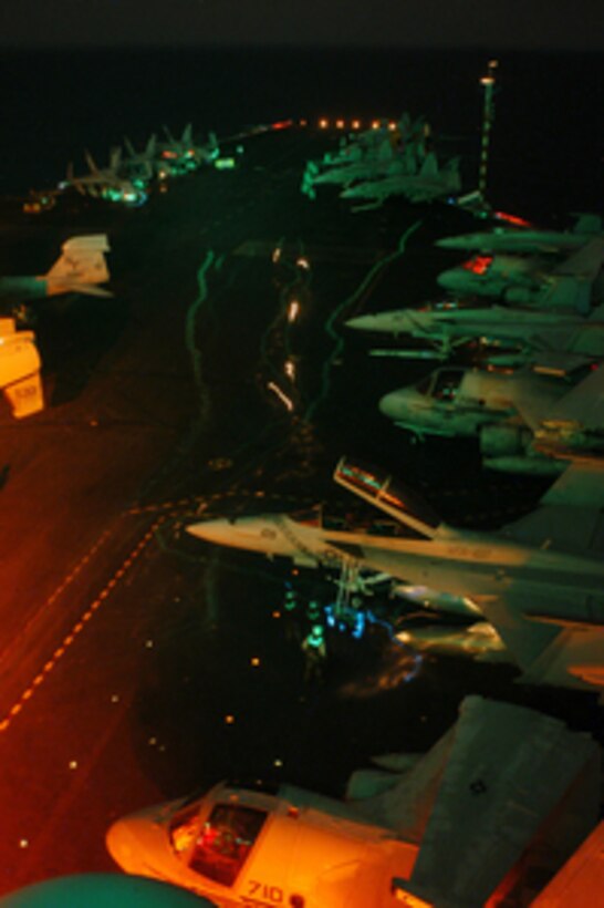 Aircraft and personnel move about under the glow of flight deck lights during night flight operations aboard the USS Kitty Hawk (CV 63) on Aug. 25, 2004. All personnel working on the flight deck wear reflective tape on flotation jackets and cranial helmets, which show as streaks of light in this time exposure. 