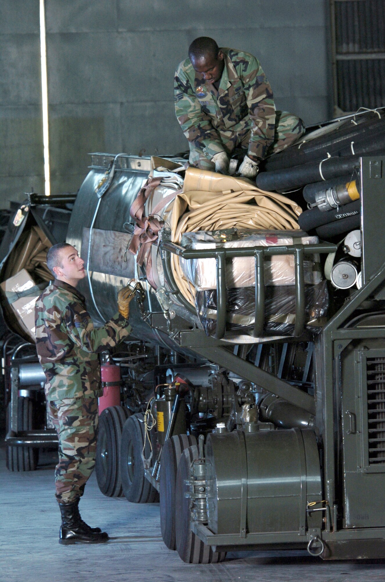 YOKOTA AIR BASE, Japan -- Senior Airmen David Cameron (top) and Michael Gullet secure cargo straps on an R-14 air transportable hydrant refueling system during an inspection here.  The R-14 can be airlifted or ground shipped anywhere in the world and made fully operational in a matter of hours.  Each unit contains a pump; two 50,000-gallon bladder tanks; and all the hoses, valves, and fittings necessary for operation.  The Airmen are assigned to the 374th Logistics Readiness Squadron's fuels mobility support equipment element.  (U.S. Air Force photo by Master Sgt. Val Gempis)

